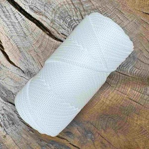 May include: A tightly wound roll of light gray yarn, resting on a weathered wooden surface. The yarn has a textured appearance, suggesting a woven or knitted construction. The neutral color and compact form indicate it's likely for crafting projects.