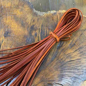 Puede incluir: Un paquete de cordón de cuero marrón, atado con un nudo, sobre una superficie de madera.