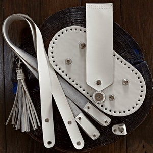 May include: White leather crafting supplies including a long strap, a small tassel, and a leather piece with holes for stitching.