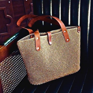 Peut inclure: Un sac fourre-tout en osier brun avec des anses en cuir et des accents métalliques. Le sac a un design tissé texturé.