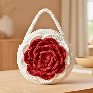 以下が含まれることがあります： 赤いバラのアップリケが付いた白いかぎ針編みのハンドバッグ。丸いバッグは、編み込みのハンドルとスカラップエッジが特徴です。手作りのバッグはユニークなアクセサリーです。