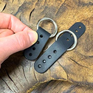 May include: Two black leather straps with silver metal rings. Each strap has five holes for adjusting the length.