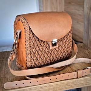 Op de afbeelding: Een bruine leren en gecrochete schoudertas met een klep sluiting en een lange verstelbare schouderband.