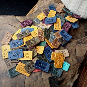 May include: A collection of brown leather labels with the text "Made with love" in various fonts and colors. The labels are scattered on a wooden surface.