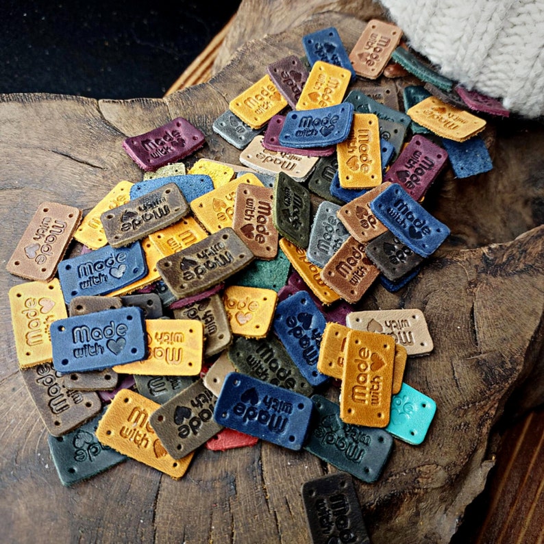 May include: A collection of brown leather labels with the text "Made with love" in various fonts and colors. The labels are scattered on a wooden surface.