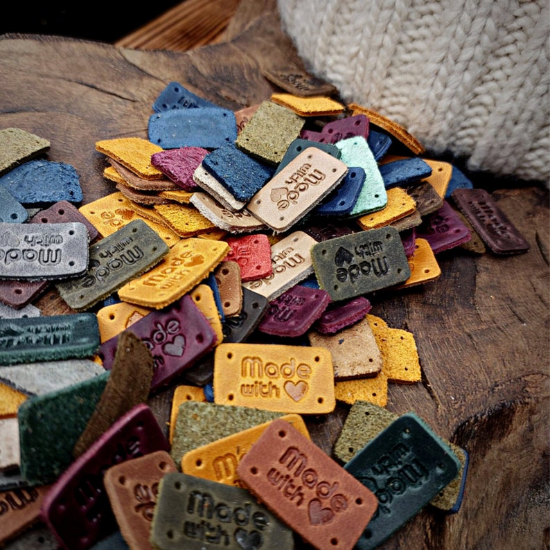 May include: A pile of colorful leather labels with the text "Made with Love" on some of them. The labels are in various shapes and sizes and have a distressed look.