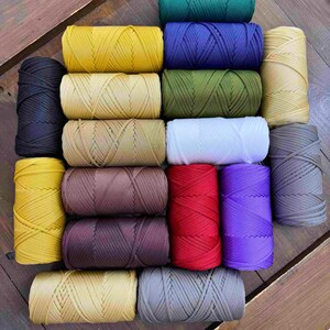 Puede incluir: Una colección de coloridas bobinas de cordón de nailon en varios tonos, incluyendo amarillo, azul, verde, rojo y morado. Los cordones están bien enrollados y dispuestos sobre una superficie de madera. Ideal para manualidades y proyectos de bricolaje.