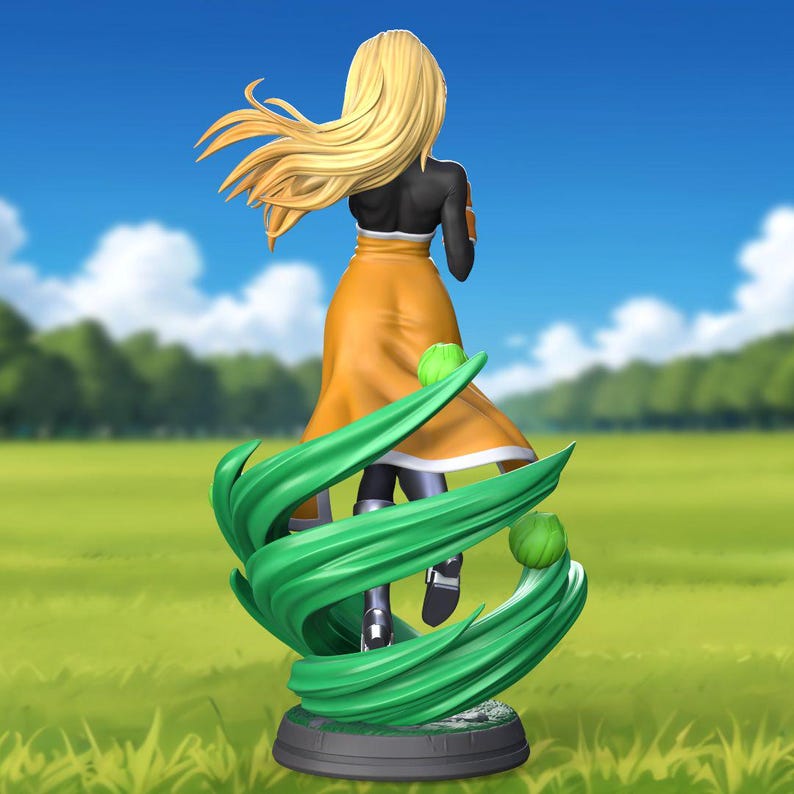 May include: A figurine of a woman with long blonde hair wearing a yellow and black dress. She is standing on a green base with swirling green accents.