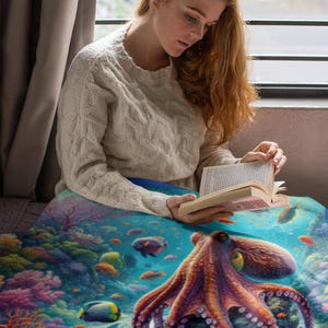 May include: A soft throw blanket featuring a vibrant underwater scene with a large purple octopus resting on a coral reef, surrounded by colorful tropical fish and diverse coral formations in shades of blue, pink, orange, and yellow.