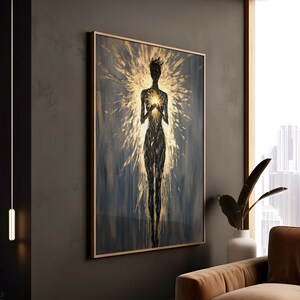 May include: Abstract art print featuring a silhouetted figure with a radiant golden aura. The artwork is framed in a light wood tone, with a dark blue and gold color palette. The figure is holding a glowing light source.