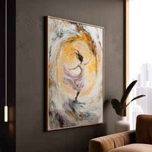 May include: Abstract art print of a dancing figure in a flowing pink dress, set against a swirling yellow and white background. The artwork is framed in a light brown wooden frame, creating a focal point for wall decor.