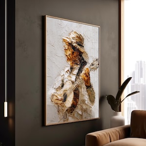 May include: Textured abstract painting of a musician playing a guitar. The artwork features a palette of white, brown, and beige tones, framed in a light wood. The painting has a thick, impasto style, creating a 3D effect.