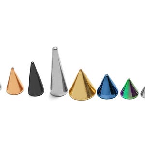 Op de afbeelding: Assortiment van negen kegelvormige metalen body jewelry-stukken in verschillende kleuren, waaronder zilver, goud, zwart, blauw en iriserend groen.