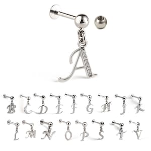 Puede incluir: Una colección de pendientes con iniciales plateadas. Cada pendiente presenta una pequeña letra colgante adornada con cristales transparentes. Las letras van de la A a la V. Los pendientes tienen un cierre de poste y bola.