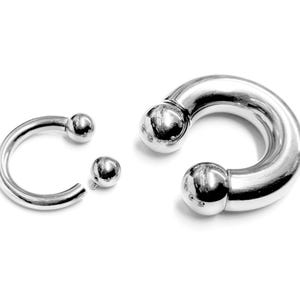 Peut inclure: Une barre de barbell circulaire argentée avec deux extrémités en boule. La barre est séparée en deux parties, montrant le filetage interne.