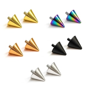 Puede incluir: Una colección de joyas corporales en forma de cono en varios colores, incluyendo oro, cobre, negro, plata y arcoíris iridiscente. Cada pieza tiene un poste roscado para una fijación segura. Las joyas se muestran sobre un fondo blanco.