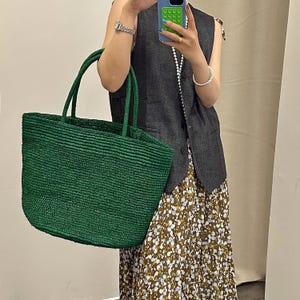 Pode incluir: Uma grande sacola tote verde esmeralda tecida com al&ccedil;as resistentes. A sacola tem formato retangular e superf&iacute;cie texturizada. A sacola &eacute; feita de material tecido, e as al&ccedil;as s&atilde;o do mesmo material. A sacola est&aacute; sendo segurada por uma pessoa.