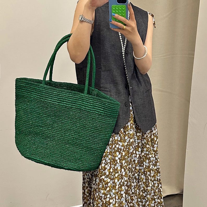 Pode incluir: Uma grande sacola tote verde esmeralda tecida com al&ccedil;as resistentes. A sacola tem formato retangular e superf&iacute;cie texturizada. A sacola &eacute; feita de material tecido, e as al&ccedil;as s&atilde;o do mesmo material. A sacola est&aacute; sendo segurada por uma pessoa.