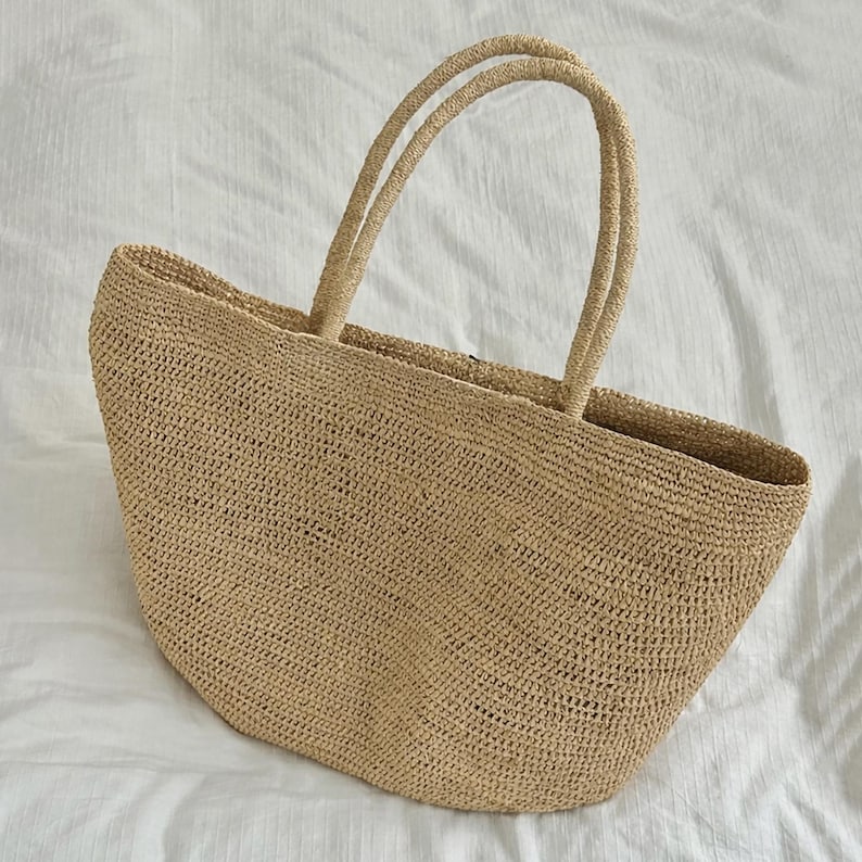 Pode incluir: Uma caneca de cer&acirc;mica branca com uma al&ccedil;a preta e o texto "But First, Coffee" em negrito preto. A caneca est&aacute; sobre um fundo desfocado, sugerindo um ambiente acolhedor.