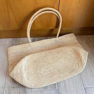 Pode incluir: Uma grande sacola tote retangular tecida em bege natural. A sacola possui duas al&ccedil;as resistentes e uma base arredondada. O padr&atilde;o de tecido &eacute; vis&iacute;vel e a sacola parece ser feita de um material de fibra natural.