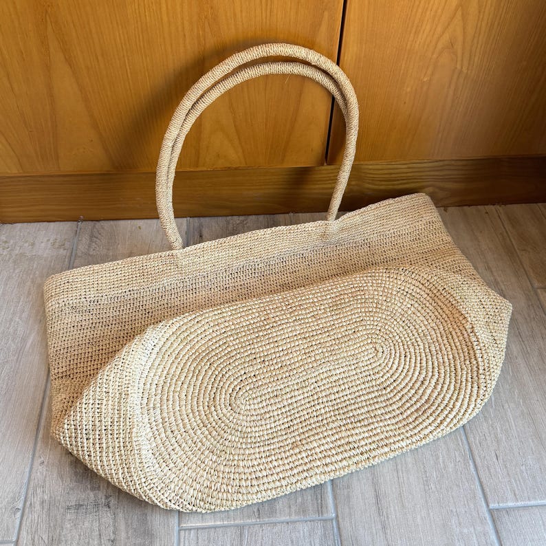 Pode incluir: Uma grande sacola tote retangular tecida em bege natural. A sacola possui duas al&ccedil;as resistentes e uma base arredondada. O padr&atilde;o de tecido &eacute; vis&iacute;vel e a sacola parece ser feita de um material de fibra natural.