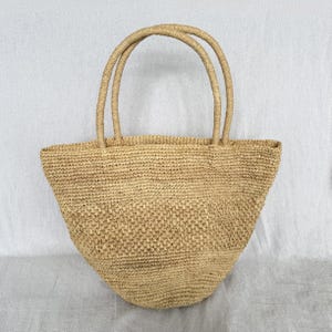 May include: A white ceramic mug with a black handle and the text "But First, Coffee" in a black, bold font. The mug is on a wooden surface. The mug is approximately 10 cm tall.