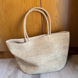 Pode incluir: Uma caneca de cer&acirc;mica branca com uma al&ccedil;a preta e o texto "But First, Coffee" em preto, com uma fonte manuscrita. A caneca est&aacute; sobre uma superf&iacute;cie branca.