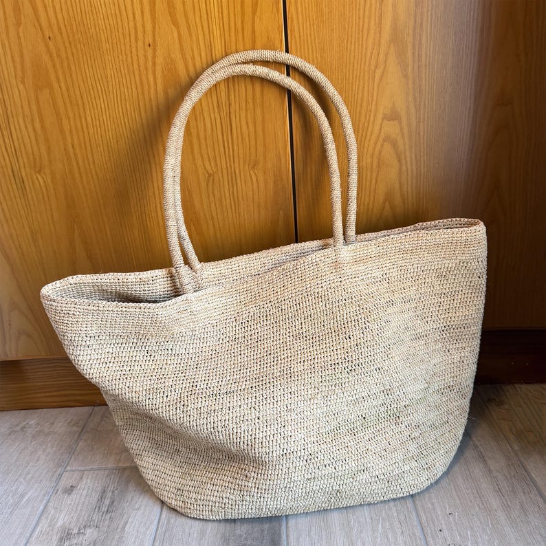 Pode incluir: Uma caneca de cer&acirc;mica branca com uma al&ccedil;a preta e o texto "But First, Coffee" em preto, com uma fonte manuscrita. A caneca est&aacute; sobre uma superf&iacute;cie branca.