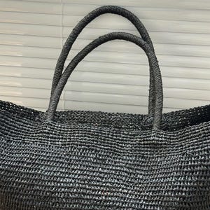 Pode incluir: Uma sacola preta tecida com duas al&ccedil;as resistentes. A sacola &eacute; feita de um material bem tecido, criando uma superf&iacute;cie texturizada. As al&ccedil;as tamb&eacute;m s&atilde;o tecidas e parecem dur&aacute;veis. A sacola &eacute; projetada para transportar itens.