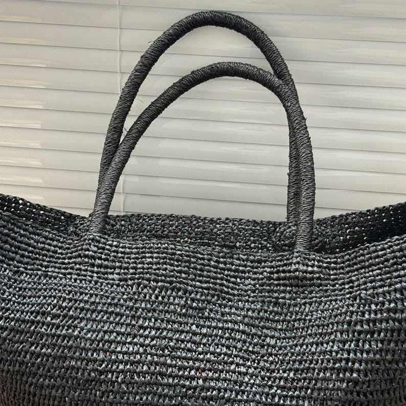 Pode incluir: Uma sacola preta tecida com duas al&ccedil;as resistentes. A sacola &eacute; feita de um material bem tecido, criando uma superf&iacute;cie texturizada. As al&ccedil;as tamb&eacute;m s&atilde;o tecidas e parecem dur&aacute;veis. A sacola &eacute; projetada para transportar itens.