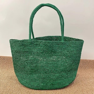 Pode incluir: Uma sacola verde tecida com duas al&ccedil;as combinando. A sacola &eacute; feita de um material texturizado e tem formato arredondado. A sacola est&aacute; vazia e fica em uma superf&iacute;cie de cor neutra.