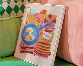 Puede incluir: Una impresión enmarcada que presenta una escena de desayuno con una sartén azul con dos huevos fritos, una pila de panqueques, una taza de café, jugo de naranja y fruta. La obra de arte tiene un fondo rosa y un marco dorado.