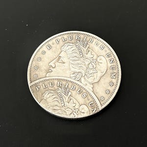Può includere: Una moneta d'argento con il profilo di una donna, circondata dalle iscrizioni «E PLURIBUS UNUM» e «LIBERTY». La moneta presenta un design dettagliato con stelle ed elementi floreali.