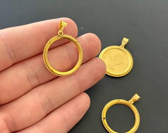 Könnte beinhalten: Goldfarbene Münzanhänger mit einem strukturierten, seilartigen Rand. Ein Rahmen wird in einer Hand gehalten, während zwei weitere auf einer dunklen Oberfläche angezeigt werden. Die Anhänger haben oben eine kleine Schlaufe für eine Kette.