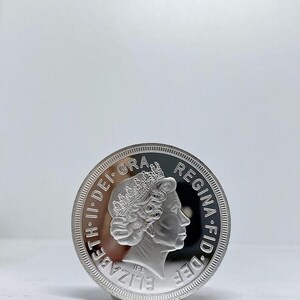 May include: A silver coin featuring a profile of a crowned person, with the inscription "ELIZABETH II DEI GRA REG F.D." around the edge. The coin has a reflective surface and is set against a plain white background.