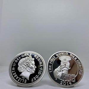 May include: Two silver coins. One features a profile of Queen Elizabeth II and the text "ELIZABETH II DEI GRA REGINA FID DEF". The other coin has a man pointing with the text "THE FIRST WORLD WAR 1914-1918 YOUR COUNTRY NEEDS YOU 2014".