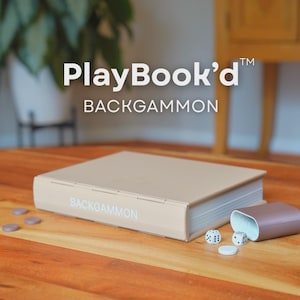 Puede incluir: Un juego de backgammon beige con el texto "PlayBook'd BACKGAMMON" sobre una superficie de madera. El juego incluye un tablero en forma de libro, dados y fichas. Un recipiente marrón contiene los dados y las fichas.