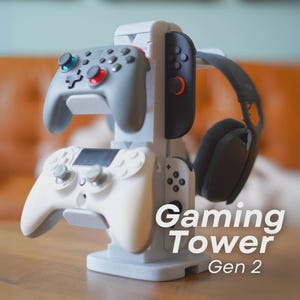 May include: A grey gaming tower displaying two game controllers, a black and grey headset, and a black game controller. The tower has the words "Gaming Tower Gen 2" printed on the front.