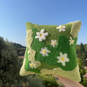 Op de afbeelding: Een groen en wit kussen met een madeliefjespatroon. Het kussen is gemaakt van een zachte, pluche stof en is perfect om elke kamer een vleugje whimsy te geven.