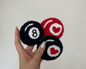 Può includere: Tre sottobicchieri circolari realizzati con tecnica punch needle e filato testurizzato. Uno raffigura una palla da biliardo nera con il numero otto bianco, uno un cerchio rosso con un cuore bianco e uno un cerchio nero con cuore bianco e centro rosso.