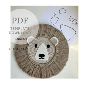 May include: A beige and white lion head wall hanging made with rope and yarn. The lion has a brown nose, black eyes, and white ears. A printable PDF template is included for the lion's face, ears, and nose.