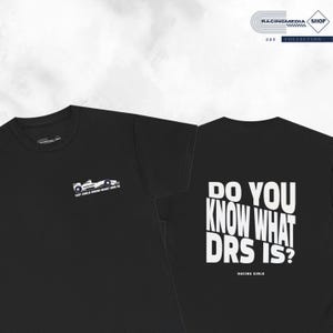 Op de afbeelding: Zwart T-shirt met een witte afbeelding van een raceauto en de tekst "WOT GIRLS KNOW WHAT DRS IS?" op de voorkant. De achterkant van het shirt heeft de tekst "DO YOU KNOW WHAT DRS IS?" in wit met de woorden "RACING GIRLS" eronder.