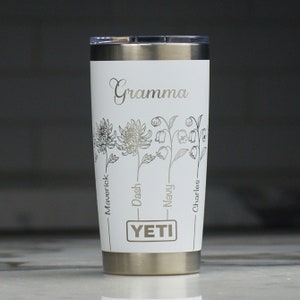 May include: White Yeti tumbler with a silver lid and a floral design. The tumbler is personalized with the word "Gramma" and the names "Maverick", "Dash", "Navy", and "Charles".