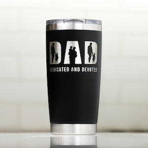May include: Black stainless steel travel mug with a silver lid. The mug has a white graphic of a father and children with the word "DAD" and the text "DEDICATED AND DEVOTED".