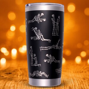 May include: Black stainless steel tumbler with a silver rim and lid. The tumbler features a repeating pattern of white skeleton illustrations in various yoga poses. The background is blurred, with an orange and brown color scheme.