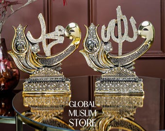 Pode incluir: Dois ornamentos decorativos de mesa com caligrafia árabe em tom dourado incrustada com cristais transparentes. Cada peça assenta numa base retangular com padrões texturizados intrincados e strass embutidos, refletindo-se numa superfície escura.