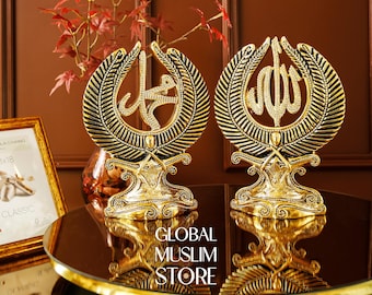Pode incluir: Dois ornamentos de mesa decorativos de cor dourada com estruturas complexas em forma de asa e caligrafia árabe central. A peça da esquerda exibe o nome Muhammad, a da direita o nome Allah, ambas decoradas com pequenos cristais transparentes.