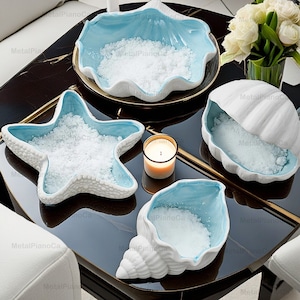 May include: Four ceramic bowls in the shape of seashells and a starfish, filled with white salt. The bowls are on a black table with a gold trim.