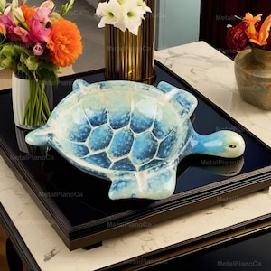 Könnte beinhalten: Eine blaue und weiße Keramik-Schale in Form einer Schildkröte mit einem strukturierten Panzerdesign. Die Schale befindet sich auf einem schwarzen Tablett mit goldener Einfassung.