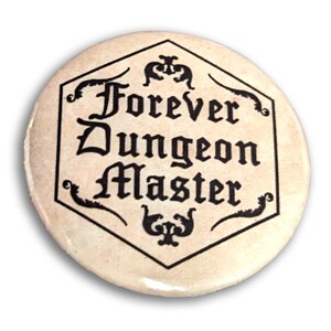 Op de afbeelding: Een beige ronde knop met een zwart zeshoekig ontwerp. De tekst "Forever Dungeon Master" is in zwart binnen de zeshoek gedrukt.